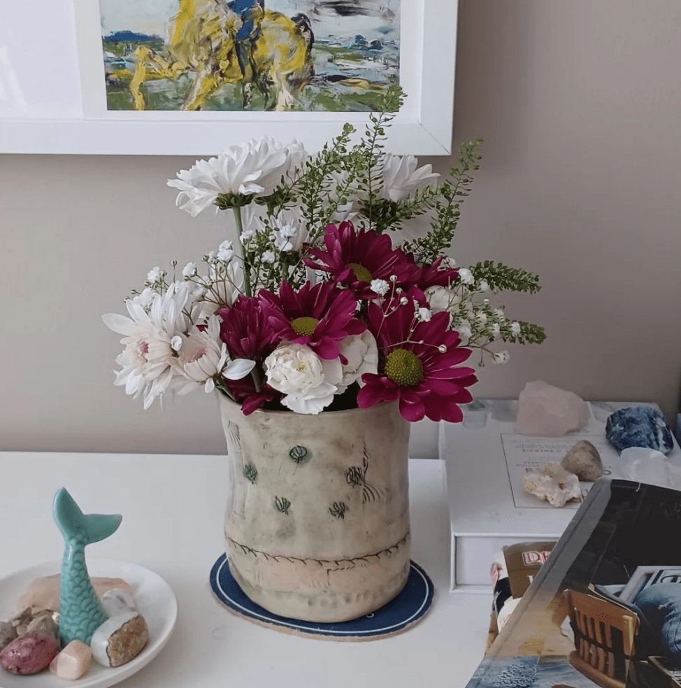 Handbuilt stoneware clay bud vase handcarved imprinted and decorated with underglaze painting holding a Spring bouquet surrounded by crystals Irish art and seaside influences.
